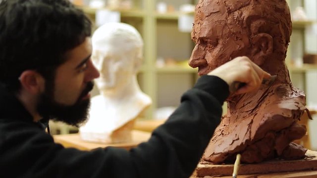 Medium shot of a Focused clay sculptor finishing a clay head in an art studio