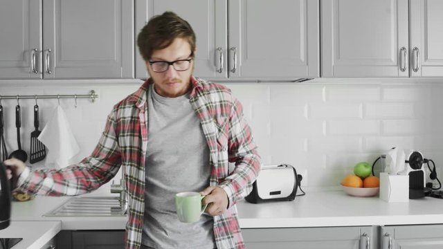 Young Man Making Tea In The Kitchen Using Kettle Tipper