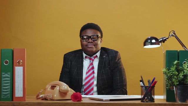 Positive afro-american trade manager in suit glasses sits at working table smiles happy successful staying in modern office corporation. Young business people.