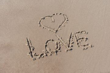 Drawn heart symbol and word love written in beach sand