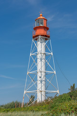 Landscape of lighthouse with red top and white base with green grass and blue sky background. Pape Lighthouse.