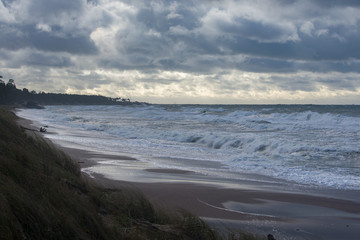 Landscape of stormy sea. Waves crashing on beach. Cloudy sky.