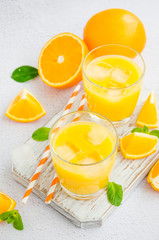 Freshly squeezed orange juice with ice in a glass with a straw on a wooden board on a light background with fresh oranges. Vertical orientation, close up.
