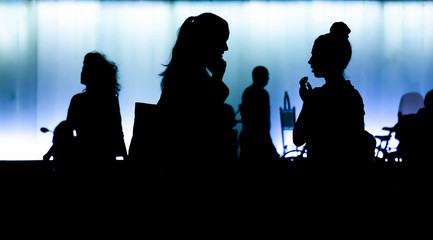 Silhouettes of two teen girls standing and talking in the night, with people walking by
