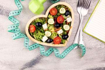 Authentic fresh salad in a wooden heart shaped cup with dumbbells excercise equipment, measuring tape on table. healthy lifestyles, good health