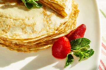 Appetizing pancakes with strawberries and mint leaves on a plate. Traditional dish for the carnival holiday. Close-up.