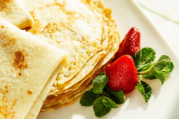 Appetizing pancakes with strawberries and mint leaves on a plate. Traditional dish for the carnival holiday. Close-up.