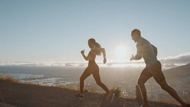 Young couple running a race on a hillside road with bright sunlight from behind. Two runners sprinting in the morning.