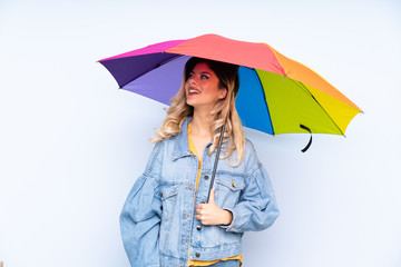 Teenager russian girl holding an umbrella isolated on blue background looking up while smiling
