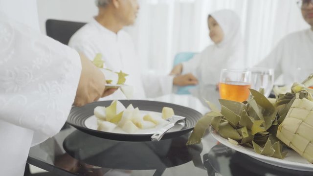 Closeup of muslim senior woman hand serving traditional foods Ketupat on the plate in the dining room at home. Shot in 4k resolution