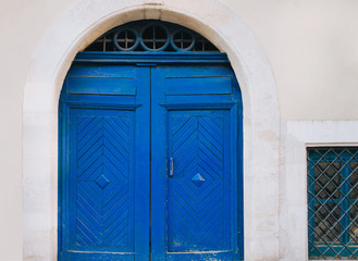 Old closed wooden blue door with diamond-shaped pattern. Facade of gray stone in the form of an arch.