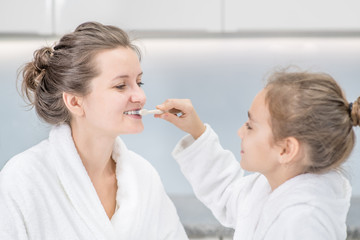 Obraz na płótnie Canvas Young girl brushes mom`s teeth with toothbrush at home