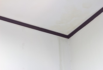 The ceiling corner with brown ceiling cornice, stains on the ceiling, rainwater stains flowing from...