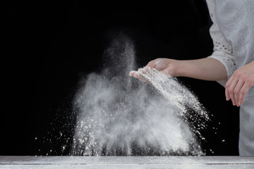 Obraz premium Kobieta posypuje mąkę na drewnianym stole, aby zrobić ciasto. Na białym tle na ciemnym tle