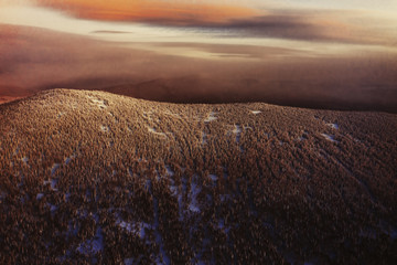 Sunset above Winter landscape aerial view, snow covered pine tree forest mountains