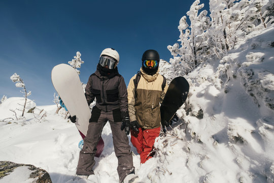 Snowboarders holding boards walking by deep snow for freeride in winter mountains. Snow covered cliffs and trees