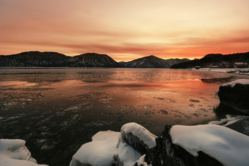 Sunset above ice covered lake, winter mountains landscape