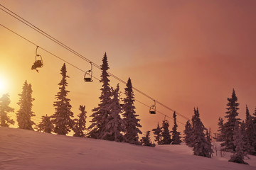 Obraz premium Ski lift in snowfall in mountains ski resort Sheregesh, Russia White winter sunset view landscape with chairlifts and snow covered fir tree forest