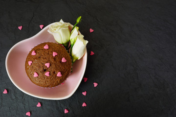 Chocolate muffin. Cake in a pink plate decorated with sugar hearts. Black table. View from above