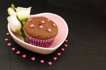 Chocolate muffin. Cake in a pink plate decorated with sugar hearts. Black table