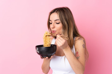 Young woman over isolated pink background holding a bowl of noodles with chopstick sand blowing it because they are hot