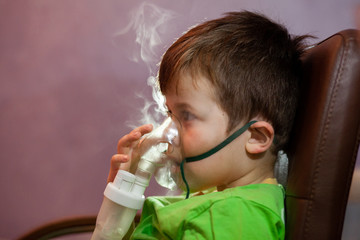 Little boy in a mask, treatments respiratory tract with a nebulizer at home. Baby sits with a...