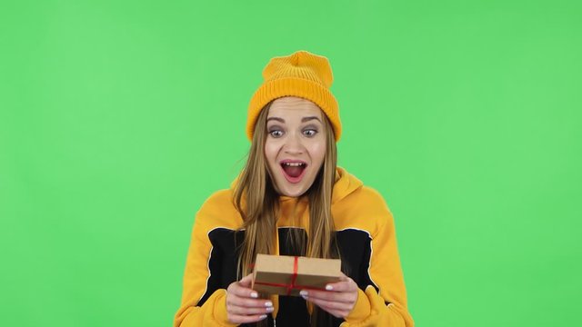 Portrait of modern girl in yellow hat is opening the gift, very surprised and rejoicing. Green screen