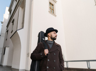 Portrait of male artist walking with guitar on the street