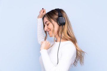 Young woman over isolated blue background listening music and dancing