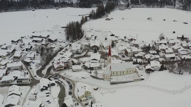 aerial view with a tilt down forward left motion of the church of holzgau austria. Beautiful view of snowy houses and church in alps