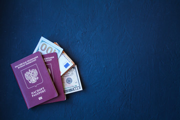 A pair of passports with dollar and Euro bills embedded in them, on a dark, dark blue background.