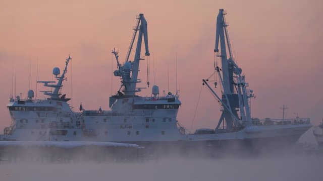 Fishing boats in the early morning at sunrise are in the port in a thick fog