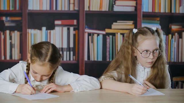 Worried small girl cribbing from paper during exam. Little schoolgirls cheating during school test. Cheating on exam concept