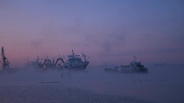 Fishing boats in the early morning at sunrise are in the port in a thick fog