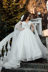 Fototapeta na wymiar Beautiful bride in a white dress goes down the stairs. Bride with elegant makeup and hairstyle. Beauty, fashion. Happiest bridal day. Enjoy every moment. Autumn 