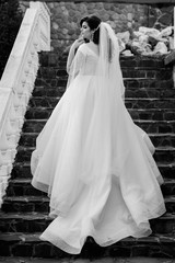 Naklejka na ściany i meble A bride in a dress climbs the stairs. Beautiful lady in a luxurious dress climbing the stairs. Graceful bride climbs stairs in a wedding day in autumn. Makeup and hairstyle in bride