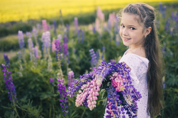 Cute girl with long hair in a white dress with flowers in her hands on nature