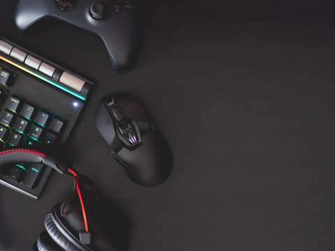 gamer workspace concept, top view a gaming gear, mouse, keyboard, joystick, headset, in ear headphone and mouse pad on black table background with copy space.