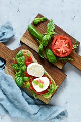 Italian Appetizer Bruschetta (toast) with Caprese Salad on a wooden board on a blue background, italian panini close up view - with fresh ingredients.