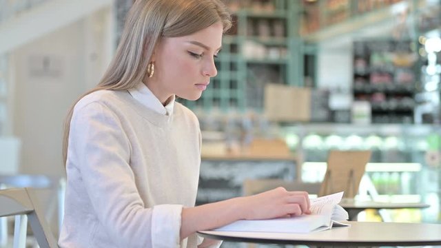 Studious Young Woman Reading Book in Cafe