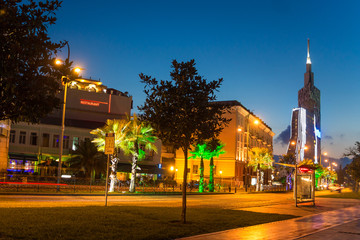 Fototapeta premium Night Seafront Promenade In European Resort Town. Evening Illuminations Light In Seaside Park In Batumi. Palm Trees And Bicycle Road.