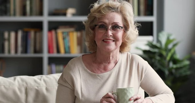 Happy older woman holding tea cup sitting on sofa, portrait