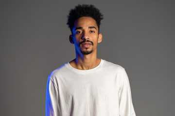 Handsome african american man with trendy curly hairdo on grey studio background. Cheerful guy smiling and looking to camera