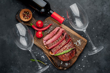 Beef steak on a cutting board with spices and a bottle of wine and glasses on a stone background with copy space for your text. Dinner concept for two