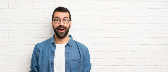 Handsome man with beard over white brick wall with surprise facial expression