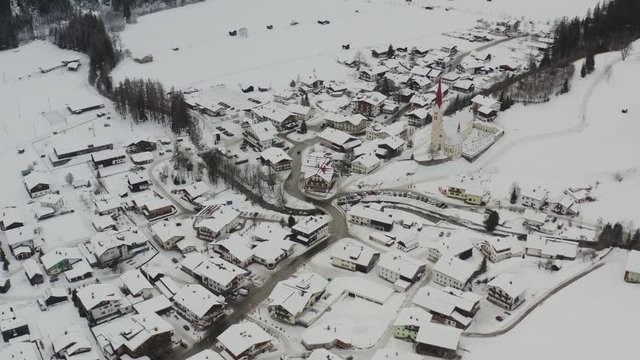 aerial view flying over the village holzgau in austria with nice church. cars driving through the village. the houses are covered with snow.