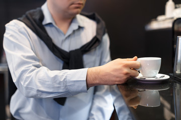 Unrecognizable adult business man in a checked shirt and cardigan behind his back reaches for an espresso cup. Morning ritual. Drinking coffee at the beginning of the day. Selective focus.