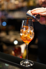 Bartender is preparing an aperol cocktail. Hand pours orange liquid into a glass of ice. Classical italian aperitif. Alcoholic beverage. Close up photo. Selective focus on glass, blurred background.