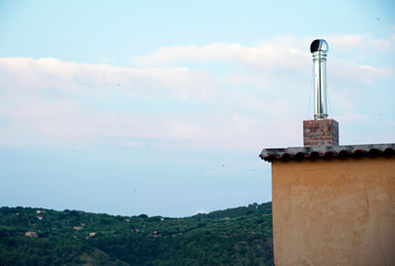 A building tiled roof with a stainless steel chimney and a hilltop in the background