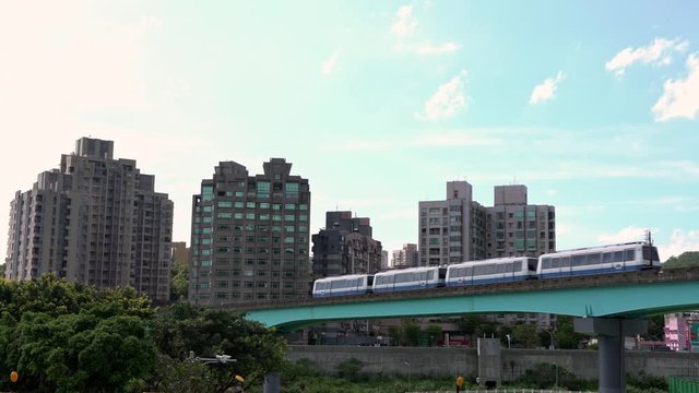 4K, Elevated train travels over a line with background of the city in Taipei. Cityscape with modern metro system arriving at the station in Taiwan. Beautiful day with blue sky.-Dan